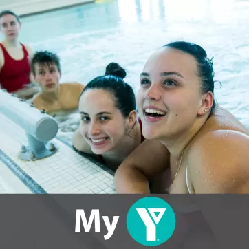 Three girls and one boy in a pool. The two girls who are closest to the camera are smiling.